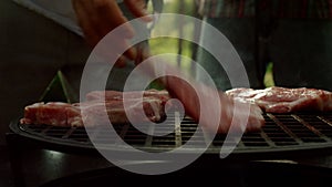 Chef putting meat slices on grate outside. Man cooking meat on grille outdoors