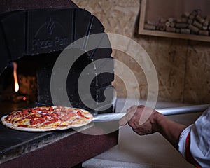 Chef putting pizza in clay oven with burning firewood photo