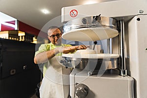chef putting pizza dough in the pressing apparatus, modern machine