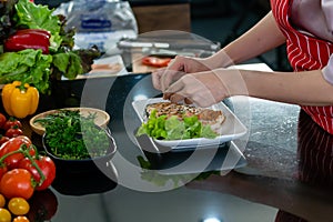 The chef is putting vegetables on a plate of salmon steaks. Take a close-up shot of the chef`s hand only