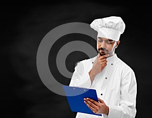 Chef reading menu on clipboard over chalkboard