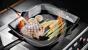 Chef in restaurant cooking flambe-style dish on frying pan. Steak with vegetables are fried with flame. Slow motion food