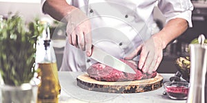 Chef in restaurant kitchen cooking,he is cutting meat or steak