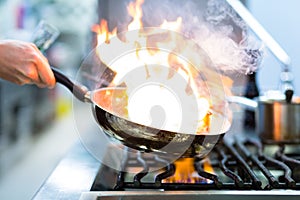 Chef in restaurant kitchen at stove with pan