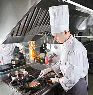 Chef in restaurant kitchen at stove with pan, cooking.