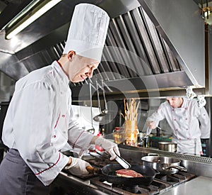 Chef in restaurant kitchen at stove with pan, cooking