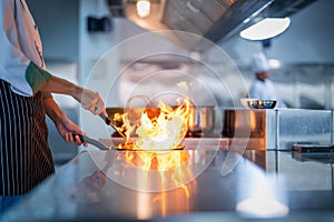 Chef in restaurant kitchen at stove and pan cooking flambe on food