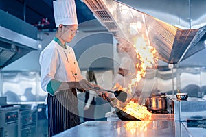 Chef in restaurant kitchen at stove and pan cooking flambe on food photo