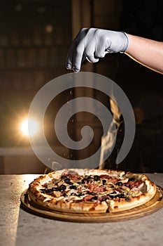 A chef with a rubber glove throws green leaves onto a hot pizza. Delivery of food and orders in the city.