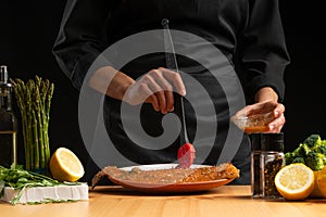 Chef rubs seafood, red fish salmon or trout marinade juice, Asian cuisine, a recipe book, on a black background. Preparing tasty