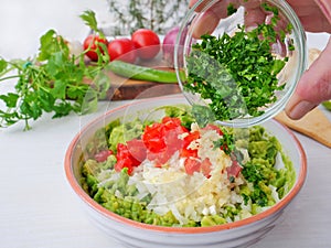 Chef`s hand adds freshly chopped cilantro to avocado dip. Making guacamole with ingredients