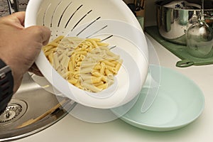 chef's hand pouring pasta from the dish drainer to later garnish