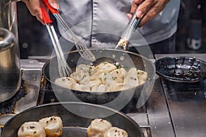 Chef`s hands cooking Chinese fried dumplings on skillet