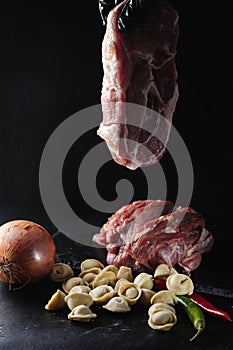 Chef`s hands hold raw meat for minced meat next to dumplings on a black background