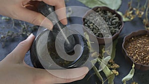 Chef`s hands using a stone mortar and pestle to confidently grind a selection of herbs and spices while making a dry