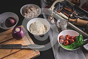 Chef`s knife, red onions, cod fish meat, rice, cherry tomatoes and olives. Ingredients for homemade fish pie. Kitchen still life