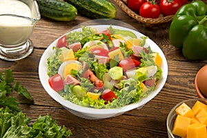 Chef salad with cheese, ham and vegetables in a white salad bowl on a wooden rustic table. Selected focus.