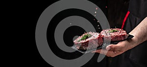 Chef salts steak in a freeze motion with rosemary and spices. Preparing fresh beef or pork on a dark background. Long banner