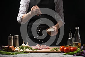 Chef salts steak grill pan. Preparing fresh beef or pork. Horizontal photo with a dark black background.