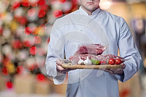 The chef shows the meat sealed in a vacuum against the background of the Christmas tree