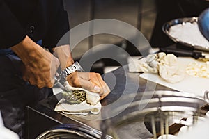 Chef shucking a fresh oyster by knife on stainless steel counter bar