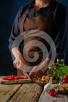 The chef slices tomatoes for the classic Caesar salad. Many ingredients from which the salad is prepared lie on the table. Festive