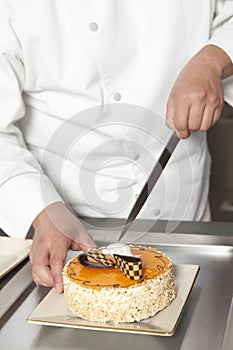 Chef Slicing Cake At Counter In Commercial Kitchen