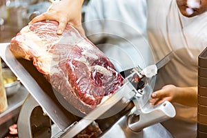 A chef is slicing a raw beef by meat slicer.