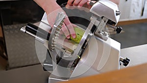 A chef slicing zucchini into slices using an industrial slicer in the kitchen.