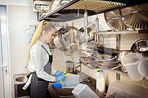 Chef of small restaurant washing dishes in sink at end of working day â€“ kitchen worker using sponge to clean dishes