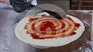 Chef is spreading Tomato Sauce on Pizza Dough with Ladle in Traditional Italian Restaurant. Italian Food