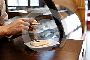 Chef sprinkled with powdered sugar sieve of a piece of cake on a plate on a wooden table