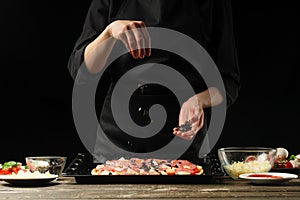 Chef sprinkles pizza with olives. Frost on the move. A concept of delicious food and healthy food. On a black background for