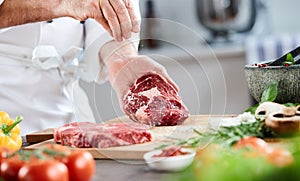 Chef sprinkling cooking salt on a raw ribeye steak
