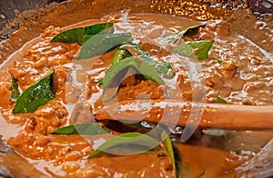 A chef stirs a creamy sauce of a Thai red chicken curry.