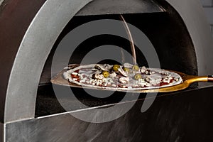 Chef taking raw pizza on metal shovel. Restaurant chef takes pizza from oven in traditional restaurant. Preparing traditional