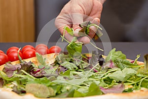 The chef throws the pizza with slices of lettuce and fresh herbs , pizza cooking