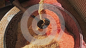 The chef tosses rice with a slotted spoon in a large cauldron while cooking pilaf