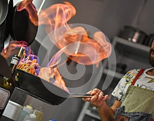 Chef tossing vegetables flambe in a pan over the burner