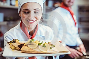 Chef in uniform in a restaurant kitchen presenting her food