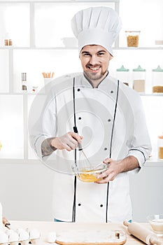 Chef in uniforms whipping eggs and milk in bowl in kitchen