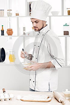 Chef in uniforms whipping eggs and milk in bowl in kitchen