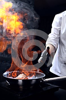 The chef uses a gas burner to cook the meat. Cooking a piece of meat. Vertical photo on a black background. Concept of a