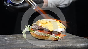 Chef using blow torch to burn cheese on tasty burger. Cook Melting slices of Cheese Using Burning Fire Stove and Making