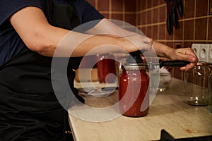 Chef using seamer or special seaming key, closes lids of jars with freshly canned tomato sauce, passata. Preserving food