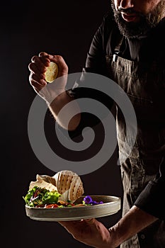 Chef watering lemon juice salad with vegetables and seafood.