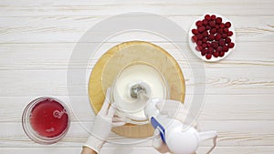 Chef whipping cream with a blender in a glass bowl. Hand in white glove. White wooden table. Raspberries in a white