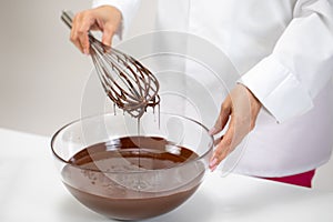Chef whisking melted chocolate in glass mixing bowl using old vintage wire whisk