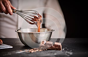 Chef whisking melted chocolate in a mixing bowl