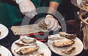 Chef in white gloves shucking a fresh oyster with knife.
